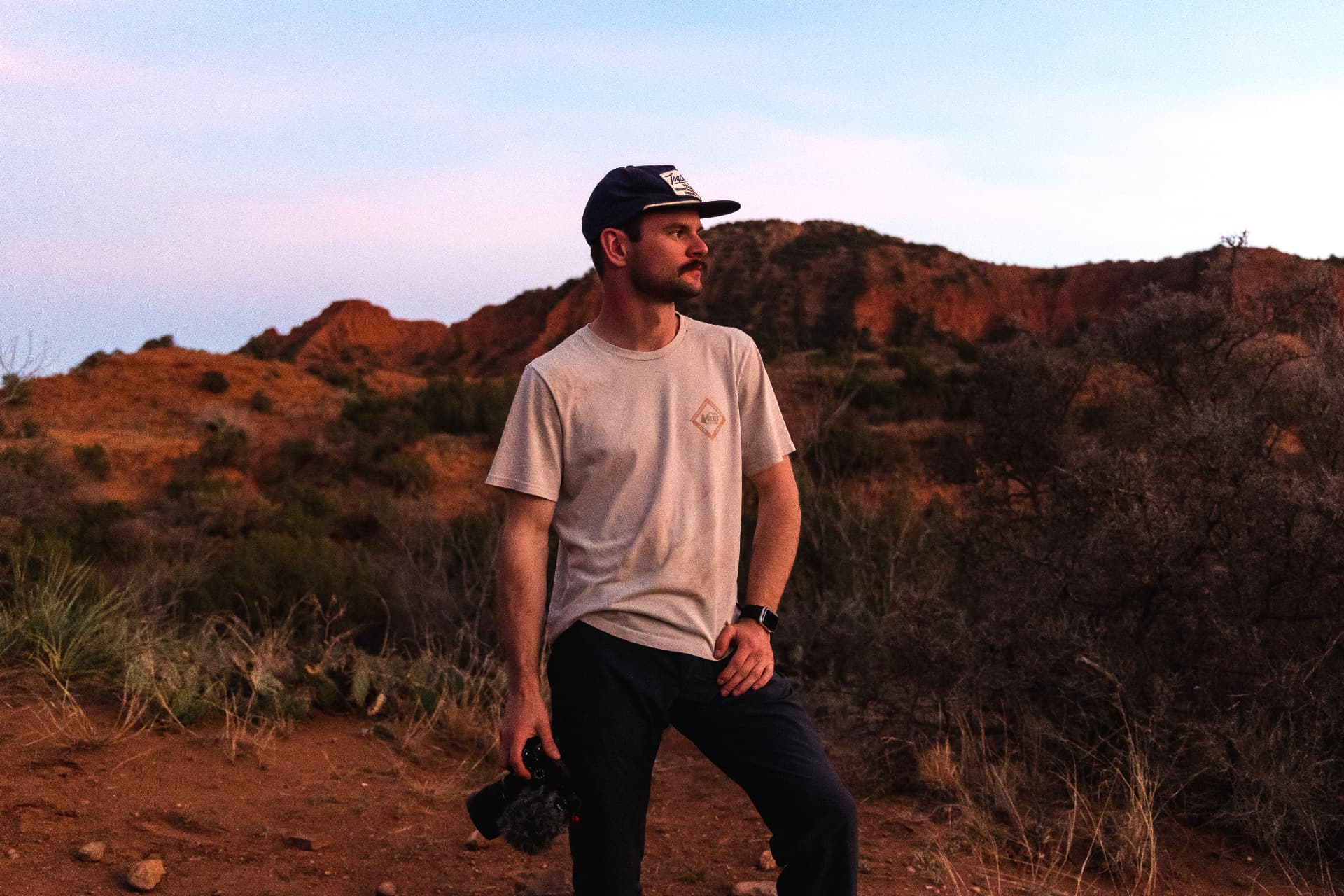Jack Karika standing in a red rock canyon at dusk, holding a camera