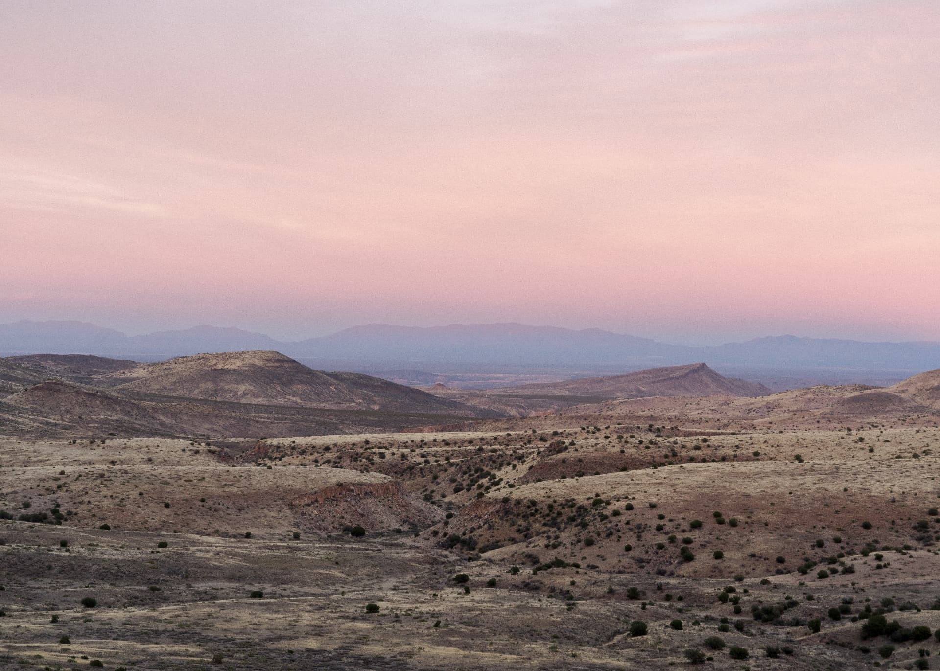 Rolling desert hills under a pink and violet dusk sky
