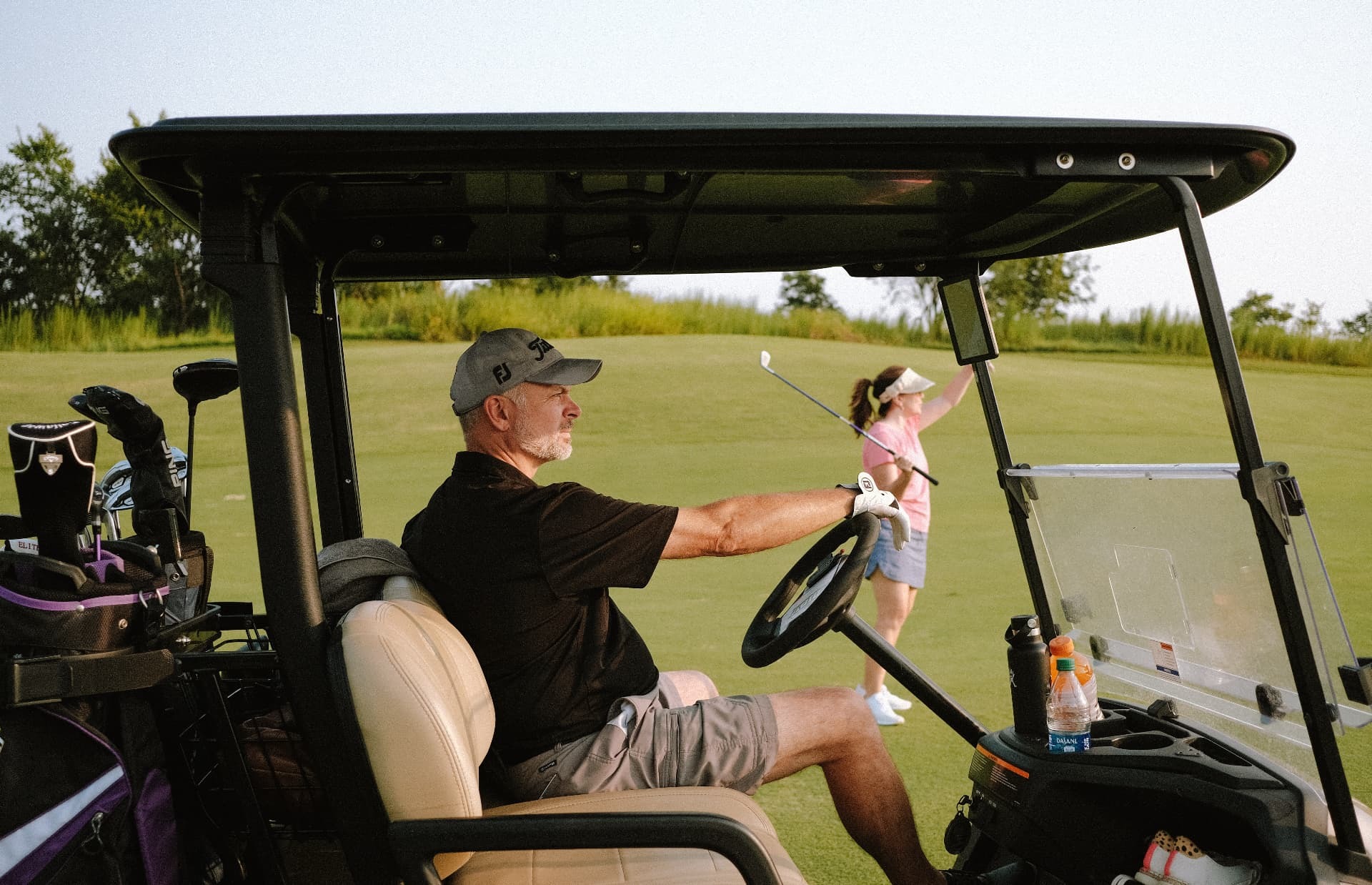 Golfer driving a cart while a player lines up a shot on the fairway