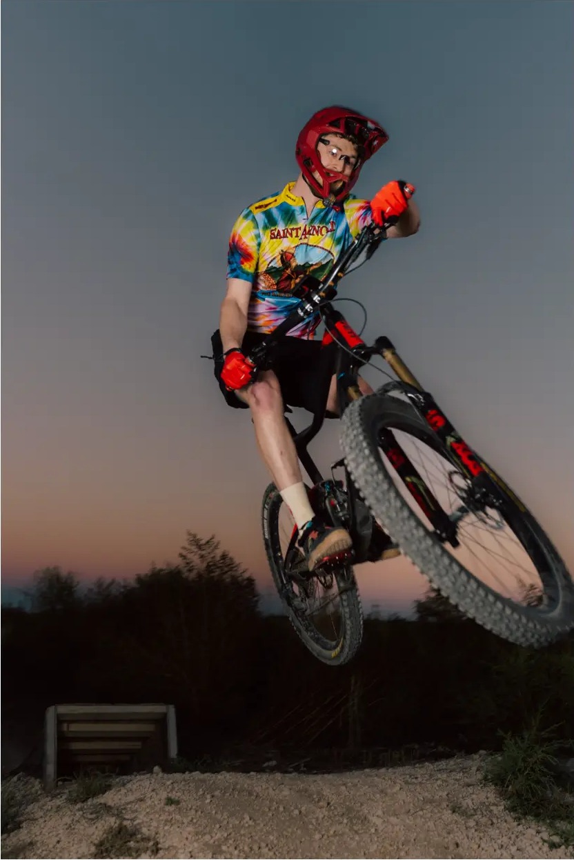 Rider in a bright jersey airborne against a dusk gradient sky