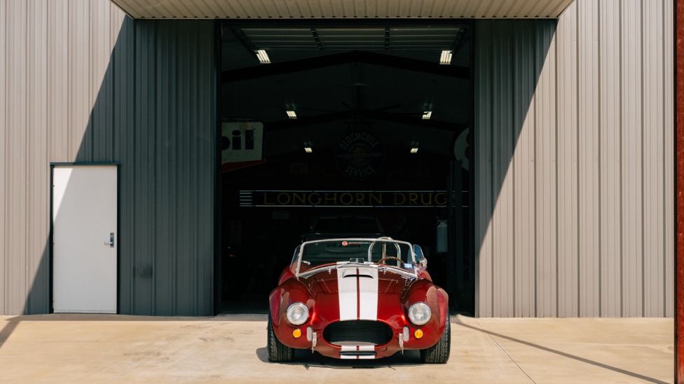 Red Cobra roadster centered in an open shop doorway