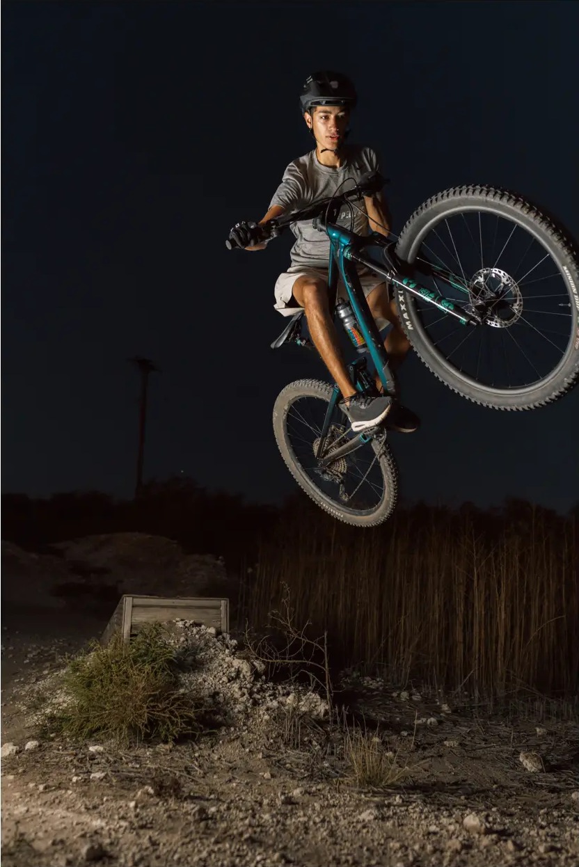 Mountain biker lit against a dark night sky mid-jump over a dirt lip