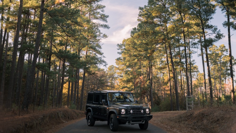 Wide view of an off-road wagon on a pine-lined road at golden hour