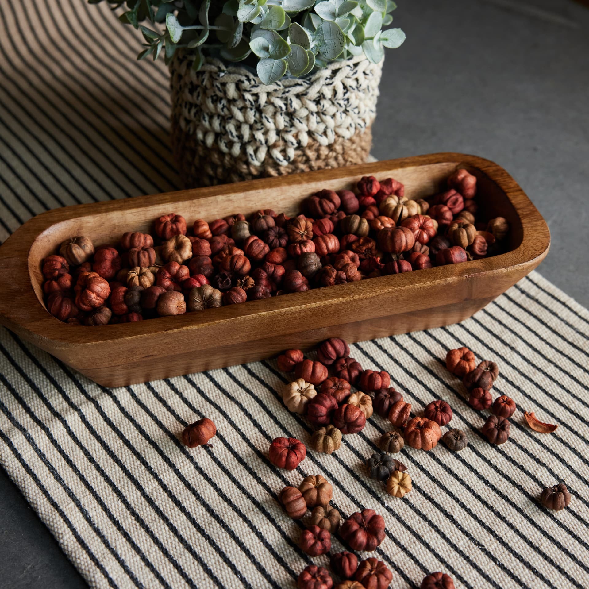 Carved wood dough bowl filled with dried mini pumpkins on a striped runner